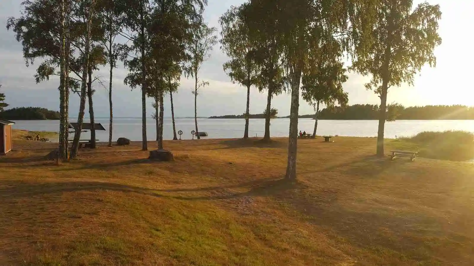 En fridfull campingplats vid Malexander med en stilla sjö i bakgrunden, omgiven av grönskande landskap och en morgondisig horisont.