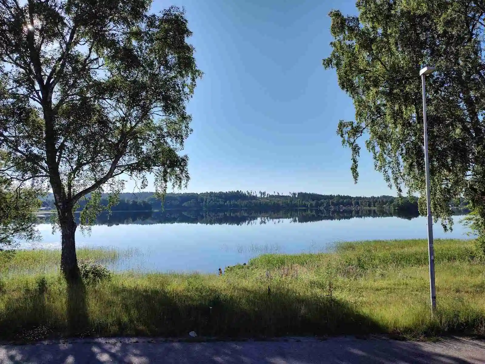 En klarblå sjö omgiven av grönskande ängar och träd i det natursköna Vegby Camping-området.