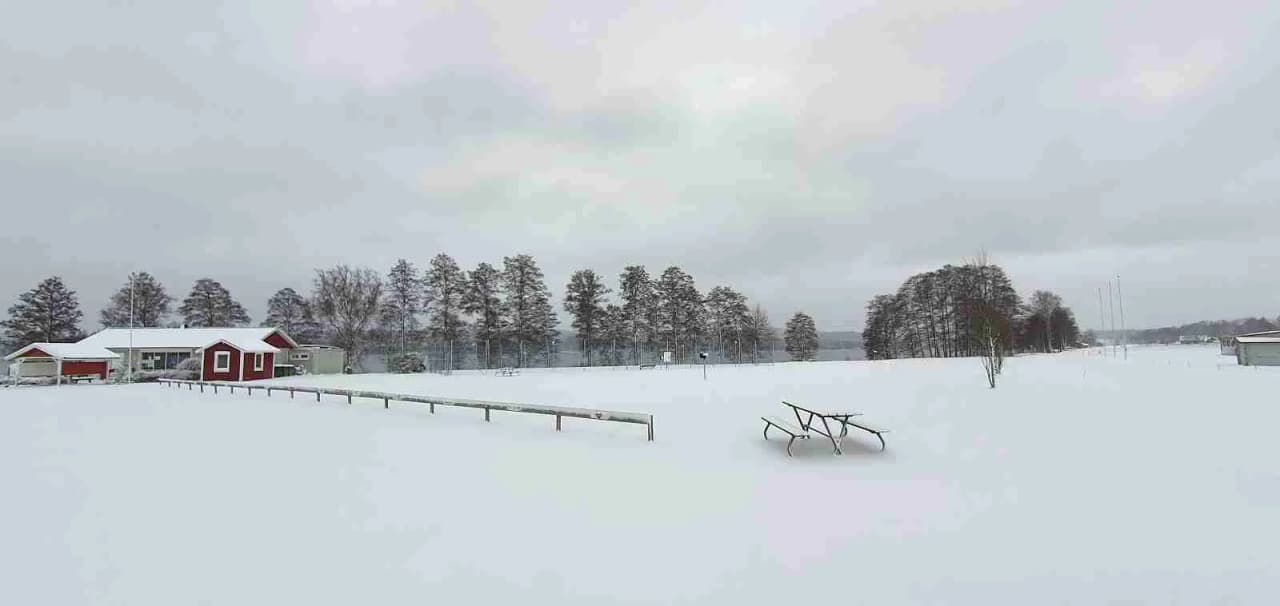 En snötäckt stuga vid Ramkvilla camping en vinterdag, omgiven av is och snö.