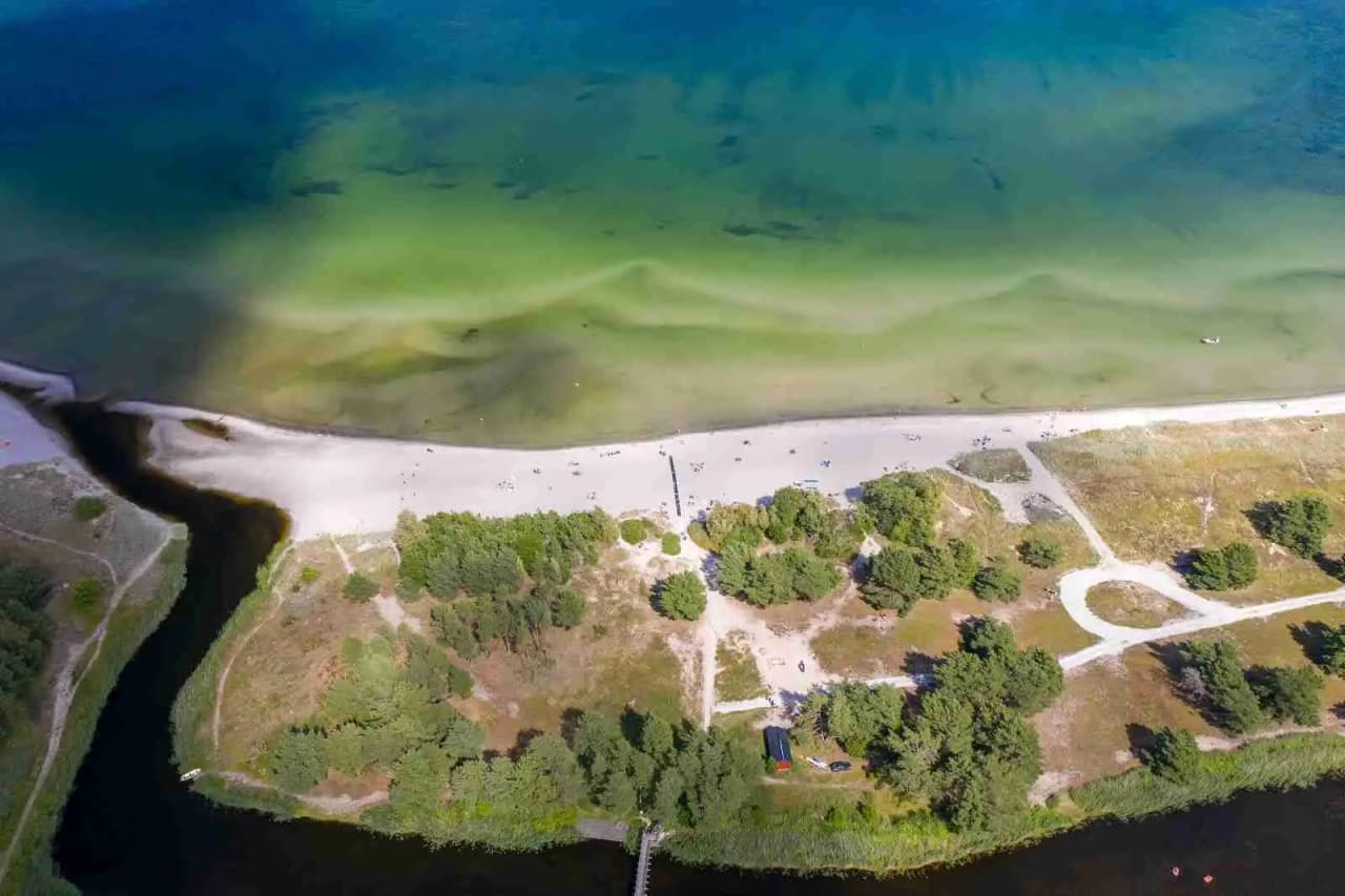 Bild av Åminne Fritid & Havsbad AB som visar en naturskön kustlinje med strand och hav. Stranden sträcker sig längs en vidsträckt bukt, omgiven av tropisk vegetation och våtmarker.