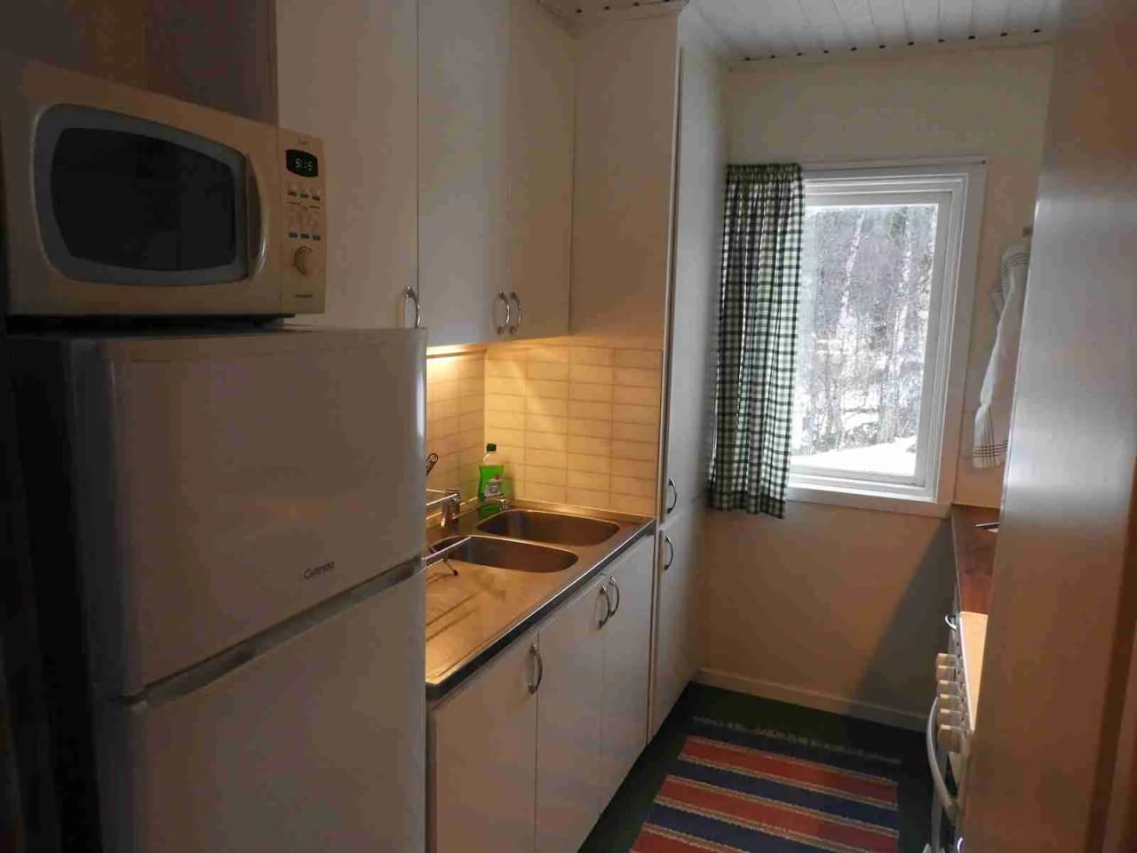 En stuga i Grönfjälls fritidsby med träinredning. Bilden visar ett kök med trägolv, diskho, kran, och hushållsapparater.