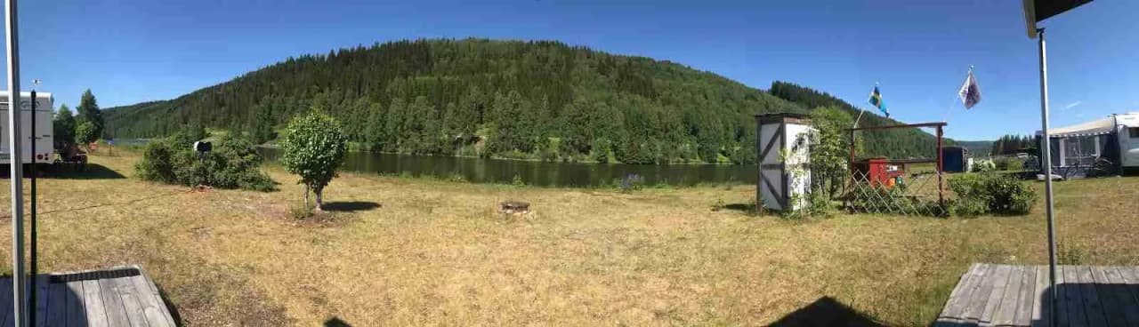 En grön och lummig campingplats omgiven av barrträd, med tält och husvagnar utspridda i det natursköna landskapet.