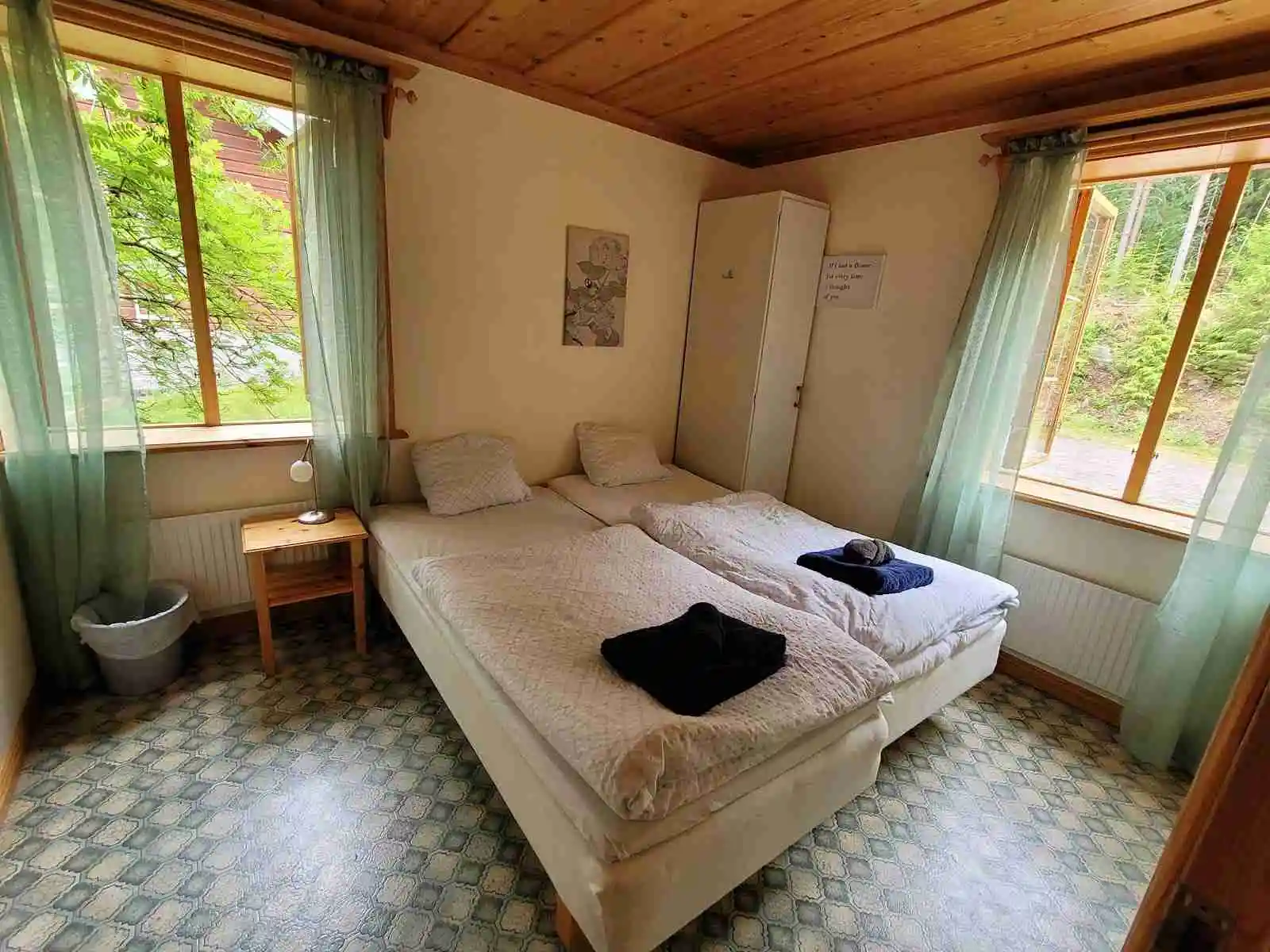 Bild på ett mysigt sovrum i trästuga på Skålsjögården Timber Lodge, med träväggar, trägolv och en enkelsäng med ljusa sängkläder.