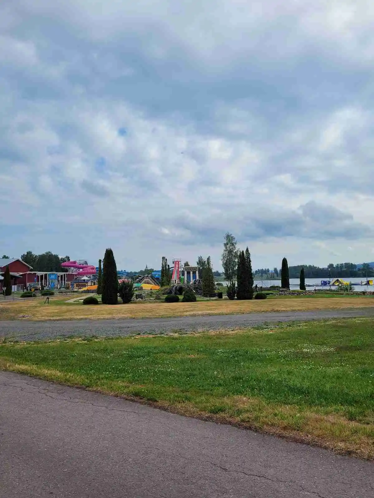 En grönskande camping och sommarland i Sunne med stora gräsmattor. Ett parkeringsområde syns, där en truck är placerad. Moln pryder himlen över parken.