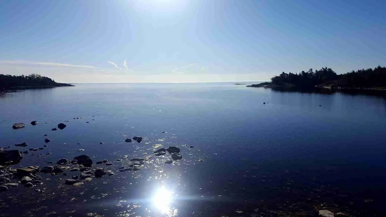 En solig dag på Norrtälje camping med utsikt över en klarblå sjö, omgiven av klippor och kustlinje.