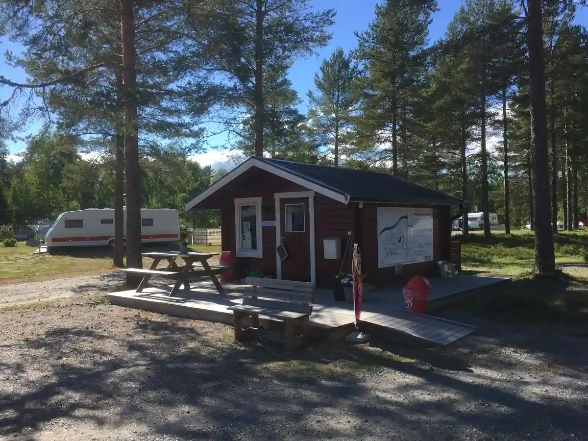 Bild av Norrmjöle camping med stugor och husbilar i bakgrunden. En stolpe och ett picknickbord står vid en grönskande gräsmatta.
