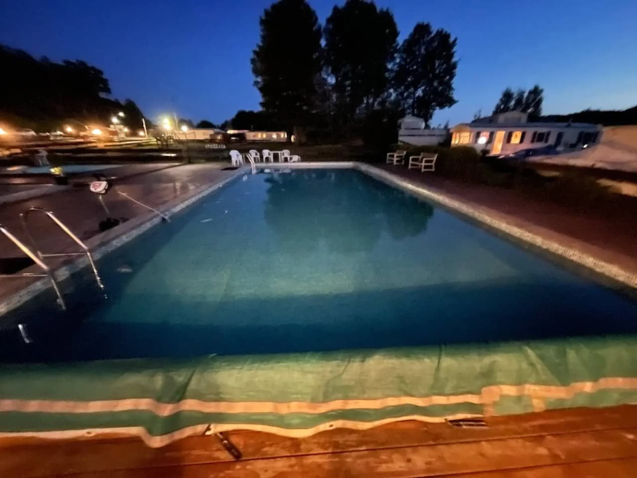 En avkopplande kvällsvy vid Ylserød Camping med en upplyst utomhuspool, omgiven av en semesterortsliknande miljö, där ljusen reflekterar i vattnet.