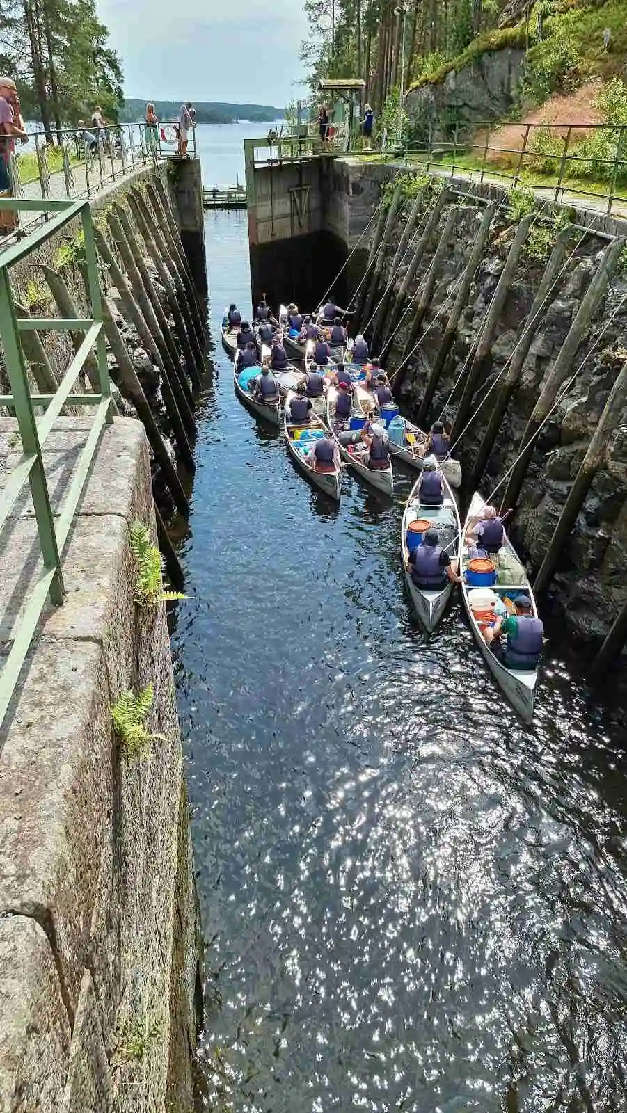 En grupp kanoter flyter lugnt på en stilla kanal omgiven av lummig grönska vid Elovsbyn Camping & Canoe, en idealisk plats för friluftsaktiviteter och paddling.