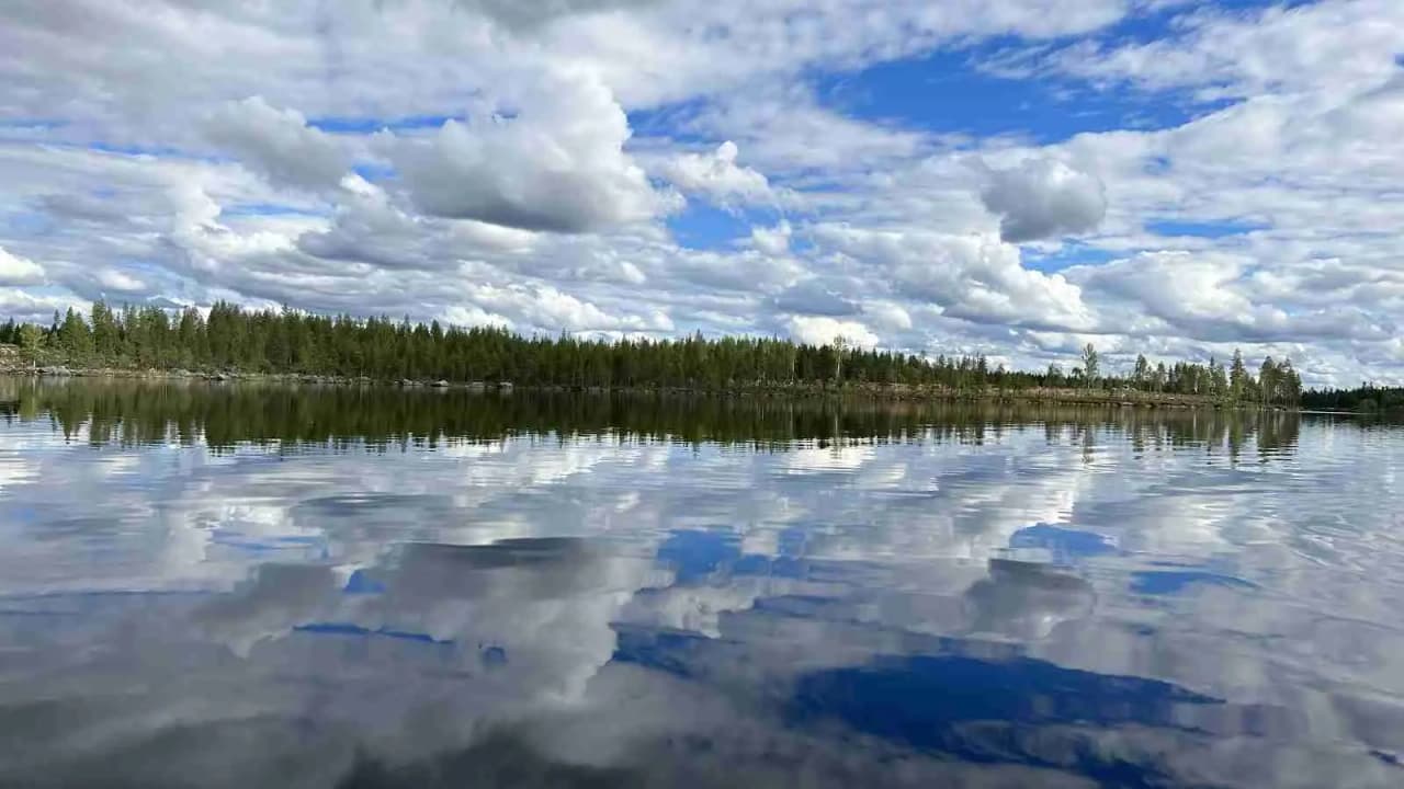 En vacker vy över Trollforsen med blå himmel och moln, där klart vatten strömmar genom en naturskön omgivning av frodig natur.