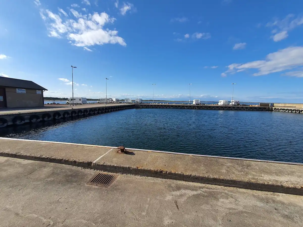 En bild av Gröndals camping & stugor, med en vy över en sjö där en brygga sträcker sig ut över vattnet. Området inkluderar en småbåtshamn med flera båtar förtöjda längs bryggan, och omgivningen är naturskön med gröna omgivningar som skapar en avkopplande atmosfär för campingbesökare.