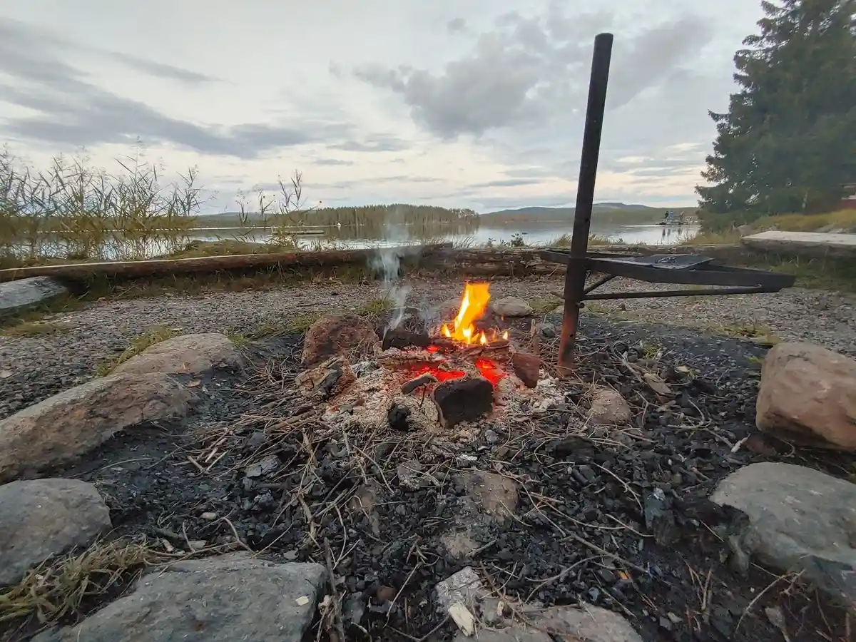 En mysig eld brinner under kvällshimlen, omgiven av glödande kol och aska, vilket ger en stämningsfull atmosfär vid Värmlandsgården.