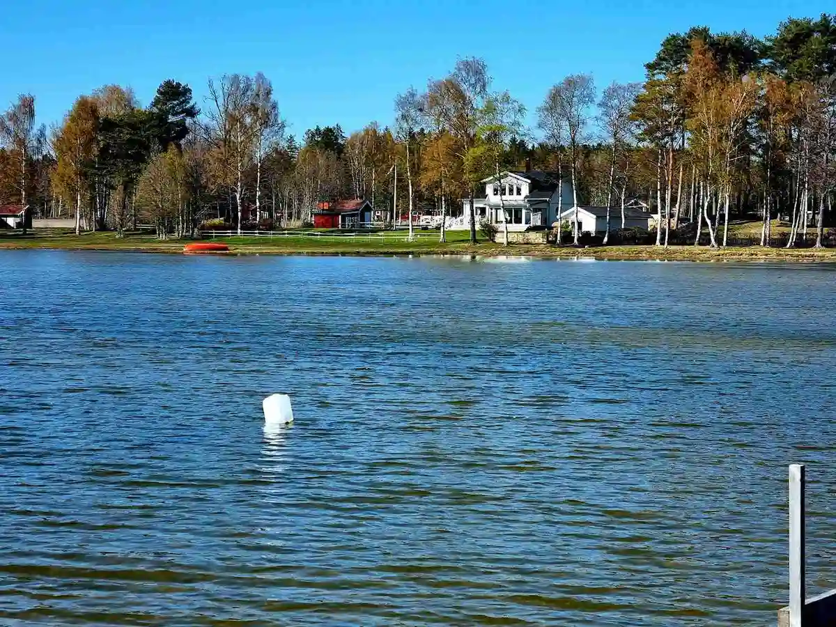 En naturskön vy över Sikhalls camping med en glittrande sjö i förgrunden, omgiven av grönskande träd och en lugn strandlinje.