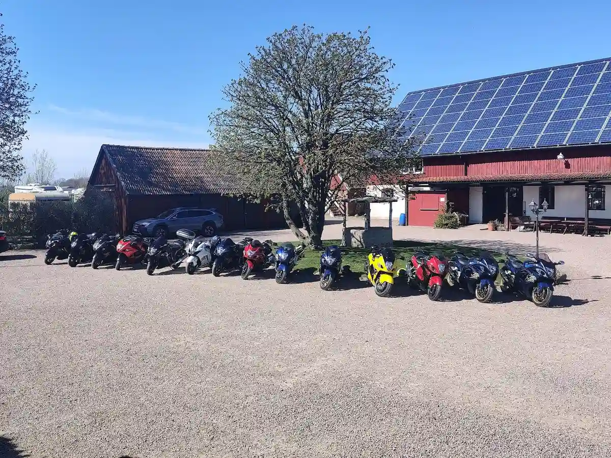 En uppställd motorcykel på Hanksville Farm, parkerad på grusunderlag. Den blanka bränsletanken och tydliga däckmönstret syns i förgrunden. I bakgrunden syns delar av en landsbygdsmiljö.