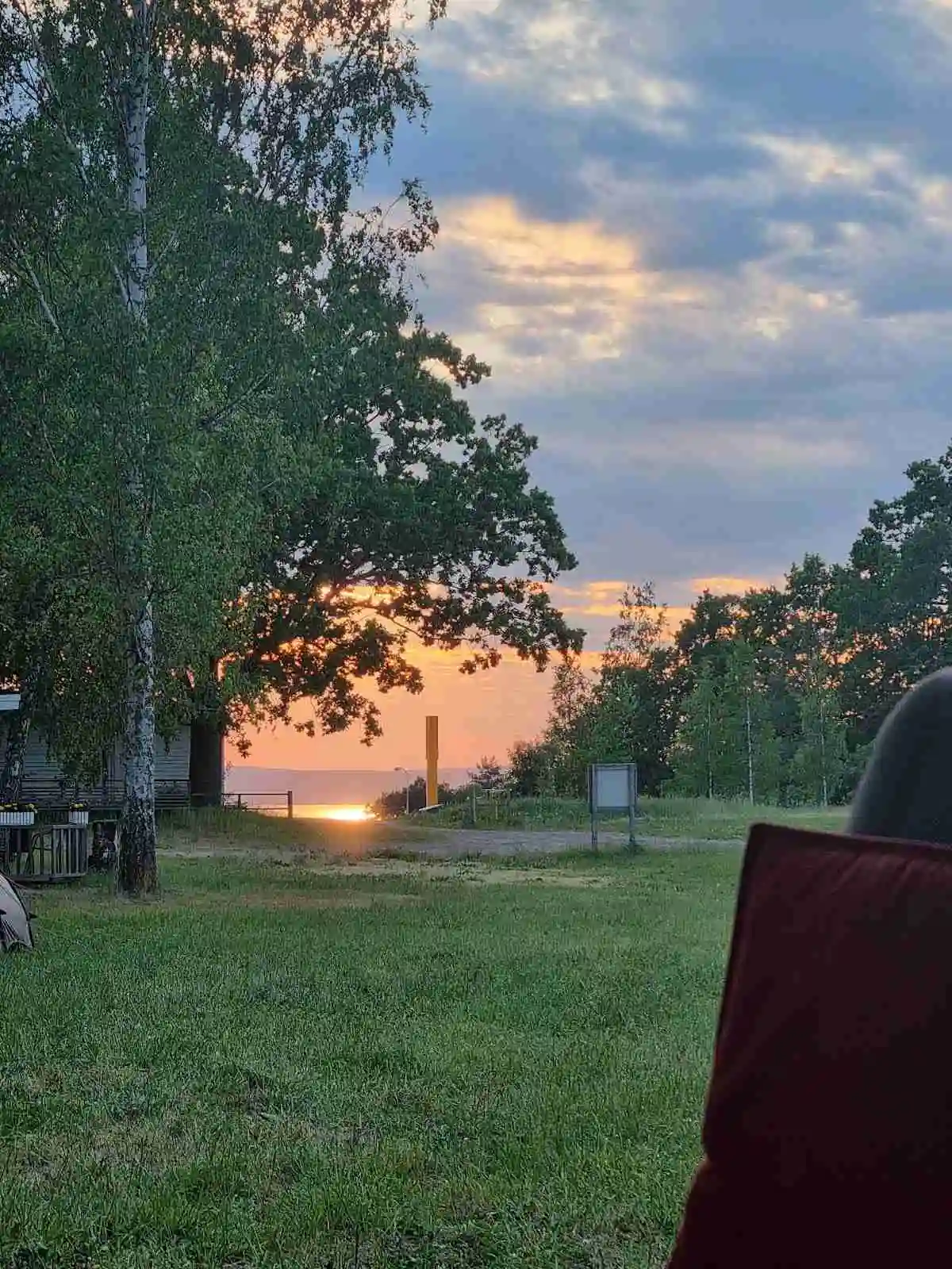 Alt-text: Utomhusmöbler på en grön gräsmatta vid camping Vättersmålen, solnedgången eller soluppgångens mjuka ljus ger en somrig atmosfär.