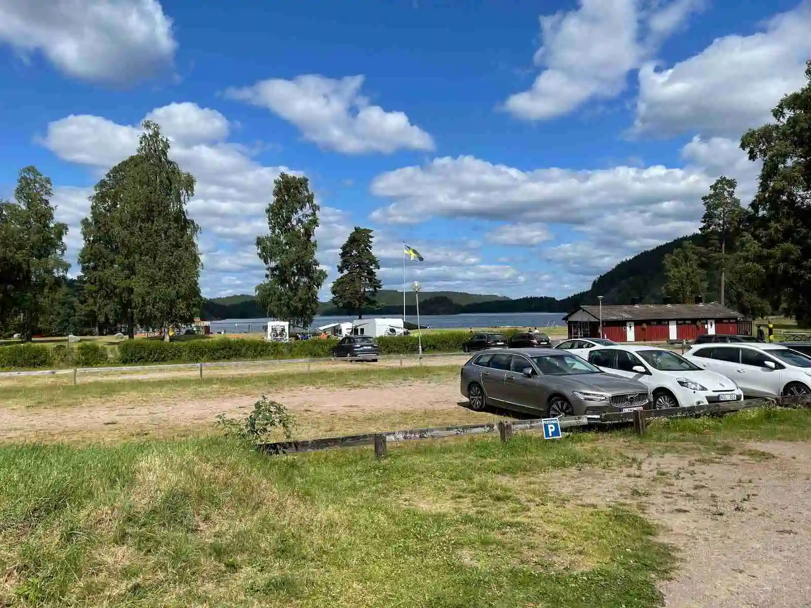 En bild av en parkeringsplats på Pinnarp Camping, fylld med olika typer av bilar under en molnig himmel.