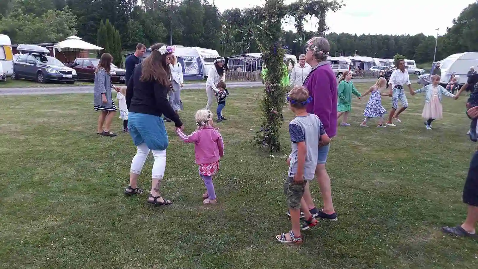 En livlig campingplats vid Österby Camping med människor som njuter av fritidsaktiviteter. Barn leker på gräset nära tält och en husbil syns i bakgrunden. Atmosfären är fylld av gemenskap och glädje.