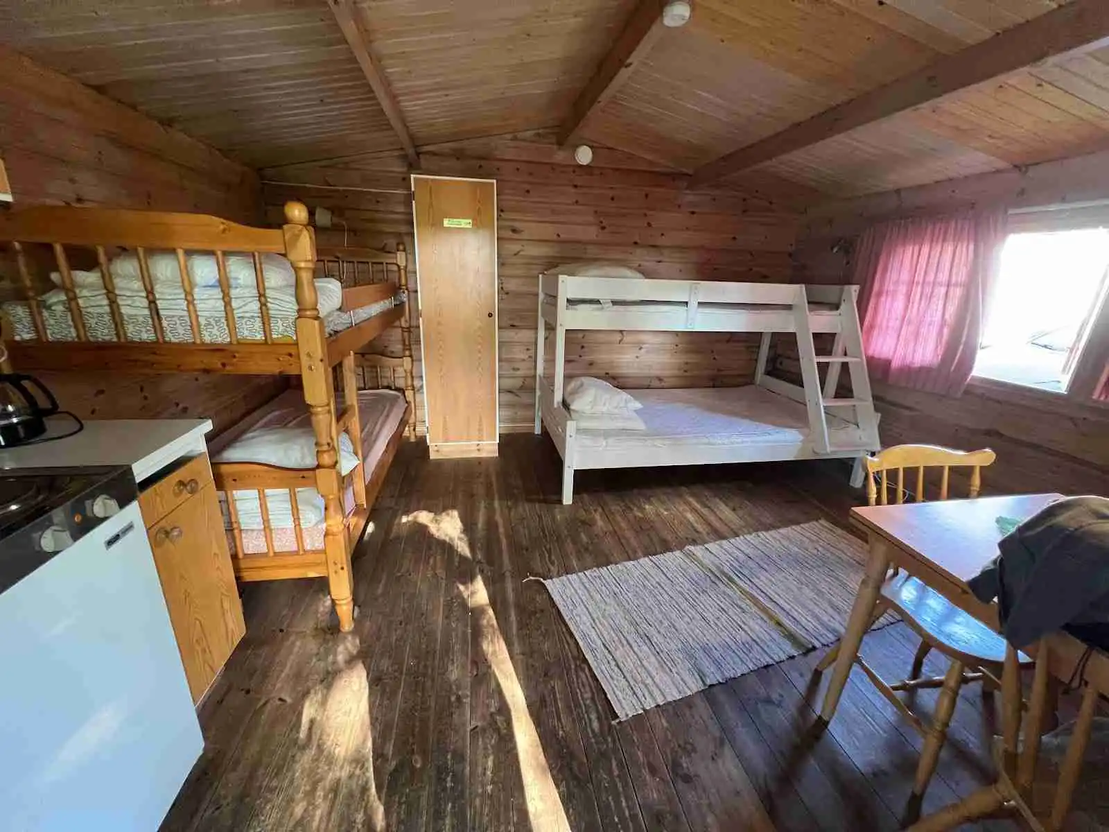 En mysig stuga med trägolv och trädetaljer inuti, enkelt möblerad med en säng och dörrar som leder ut till naturen vid Sikhalls camping.