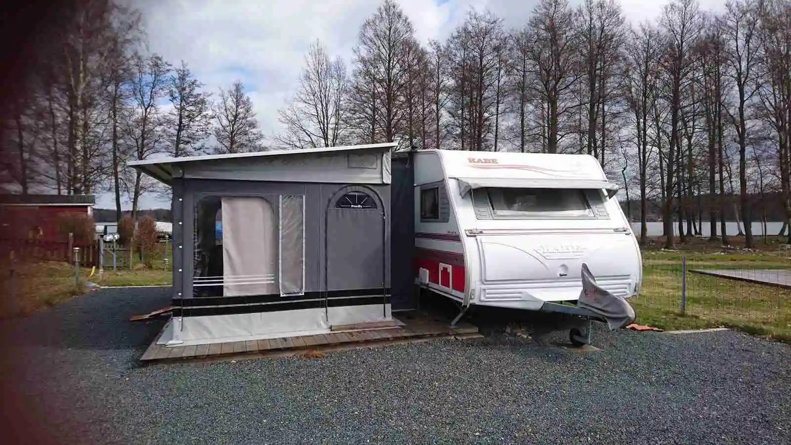 Bild av en husvagn och husbil parkerade på Österby Camping, omgiven av grönska och träd.