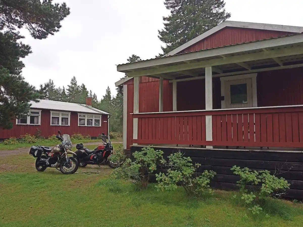 En charmig stuga med träpanel och sadeltak, omgiven av en rymlig trädgård i Tivedens natursköna landskap. En välkomnande veranda syns på framsidan.