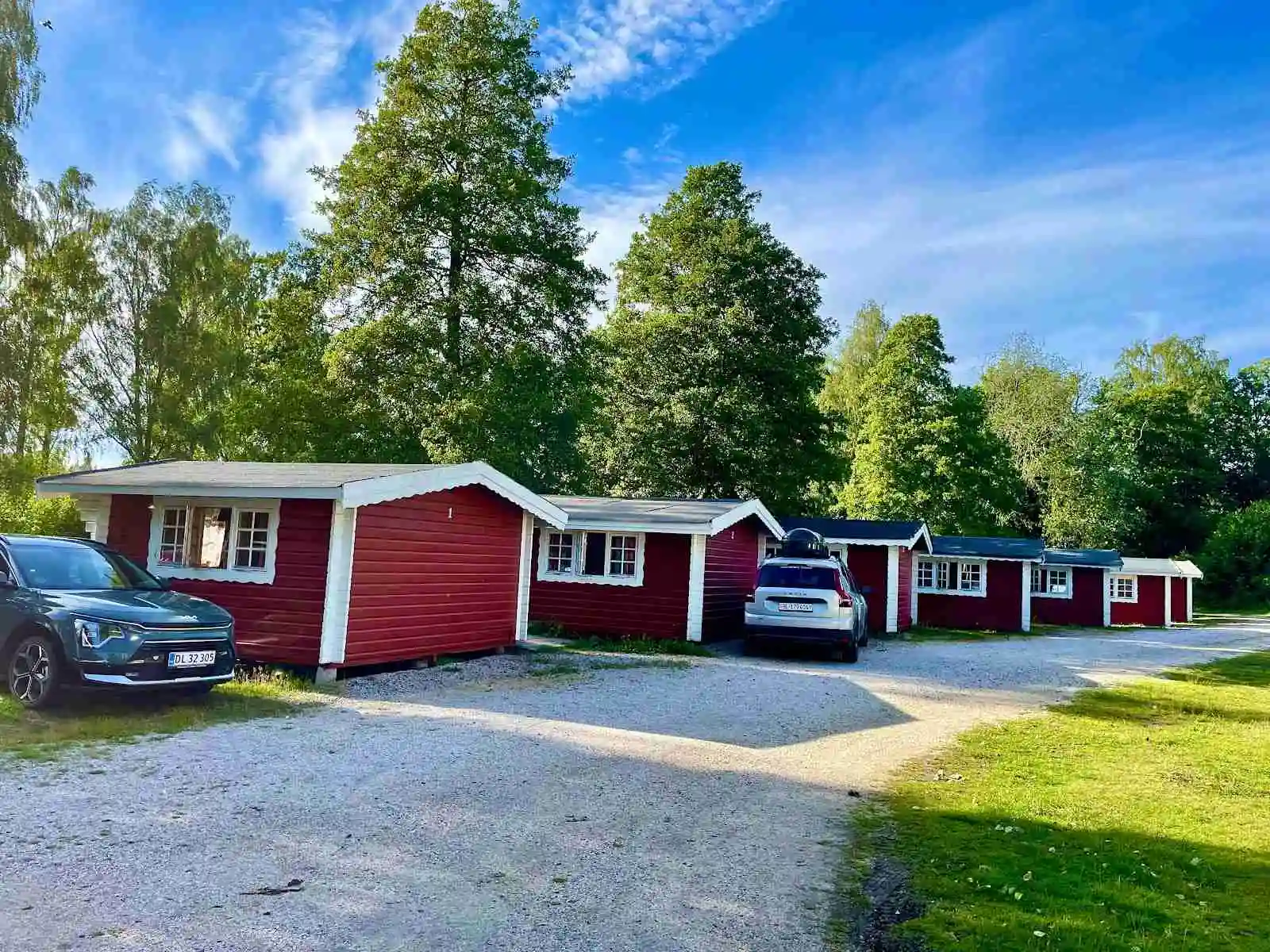 Bild av en stuga vid Sikhalls camping med flera parkerade bilar i olika storlekar längs en grusad uppfart.