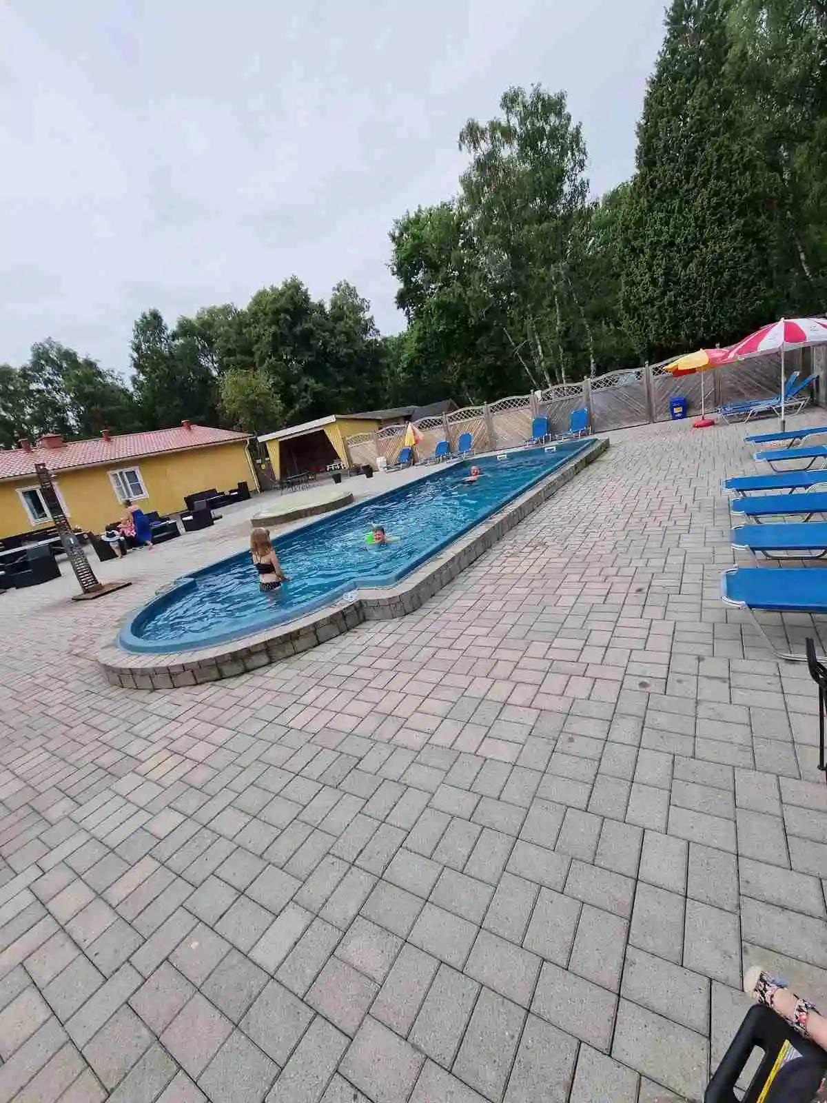 En solig dag på Ronneby Havscamping med en inbjudande swimmingpool omgiven av solstolar och parasoller, perfekt för avkoppling och semester.