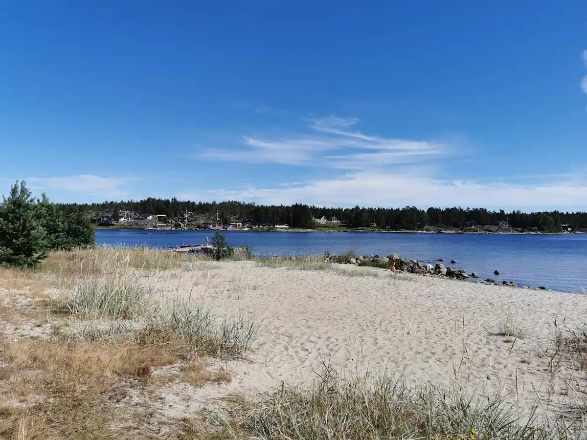 En solig dag vid Ava havsbad med klarblått vatten och en sandstrand i förgrunden.