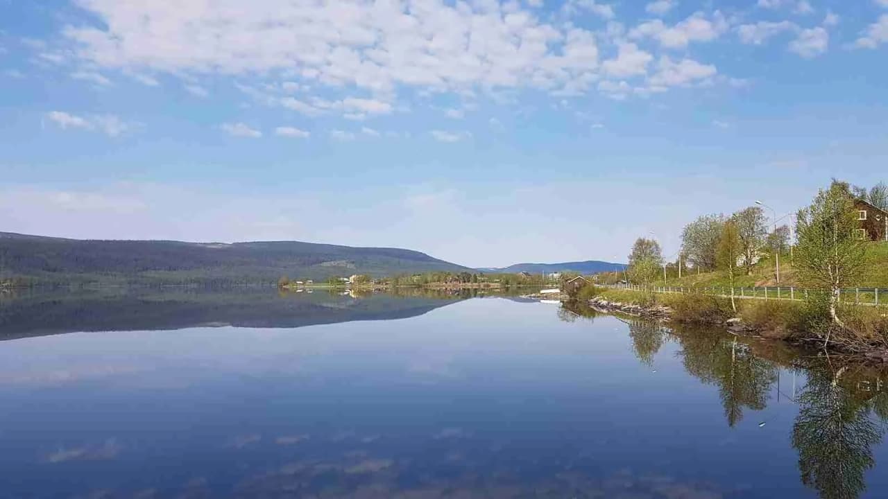 Alt-text: Vy över Storsjö camping och ställplats, med vattenresurser och en vattenväg i förgrunden, omgiven av bergsformationer och natursköna kullar.