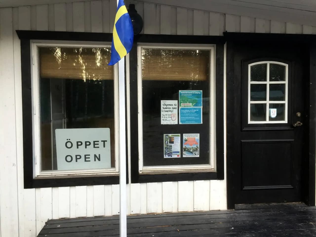 En campingentré vid Vuollerim med en skärmdörr och fasad av kompositmaterial. En skylt vid sidan av dörren visar information om platsen.