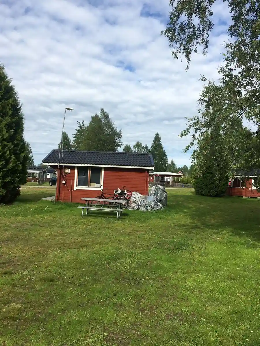 Bilden visar en liten stuga omgiven av en välskött gräsmatta och trädgård vid Camp Kungsgården.
