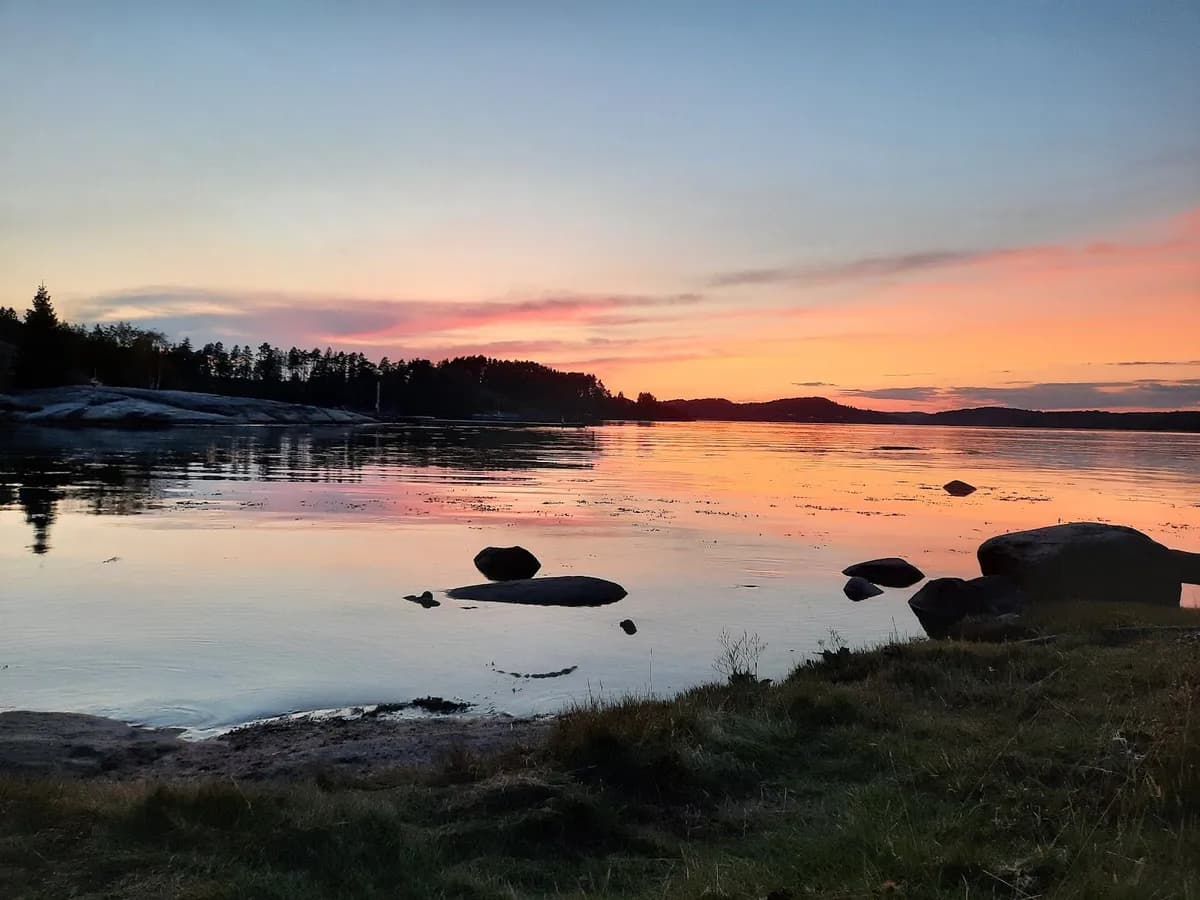 En vacker solnedgång vid Almöns Bad & Camping, med horisonten i bakgrunden och ett stilla vattendrag kantat av klippor.