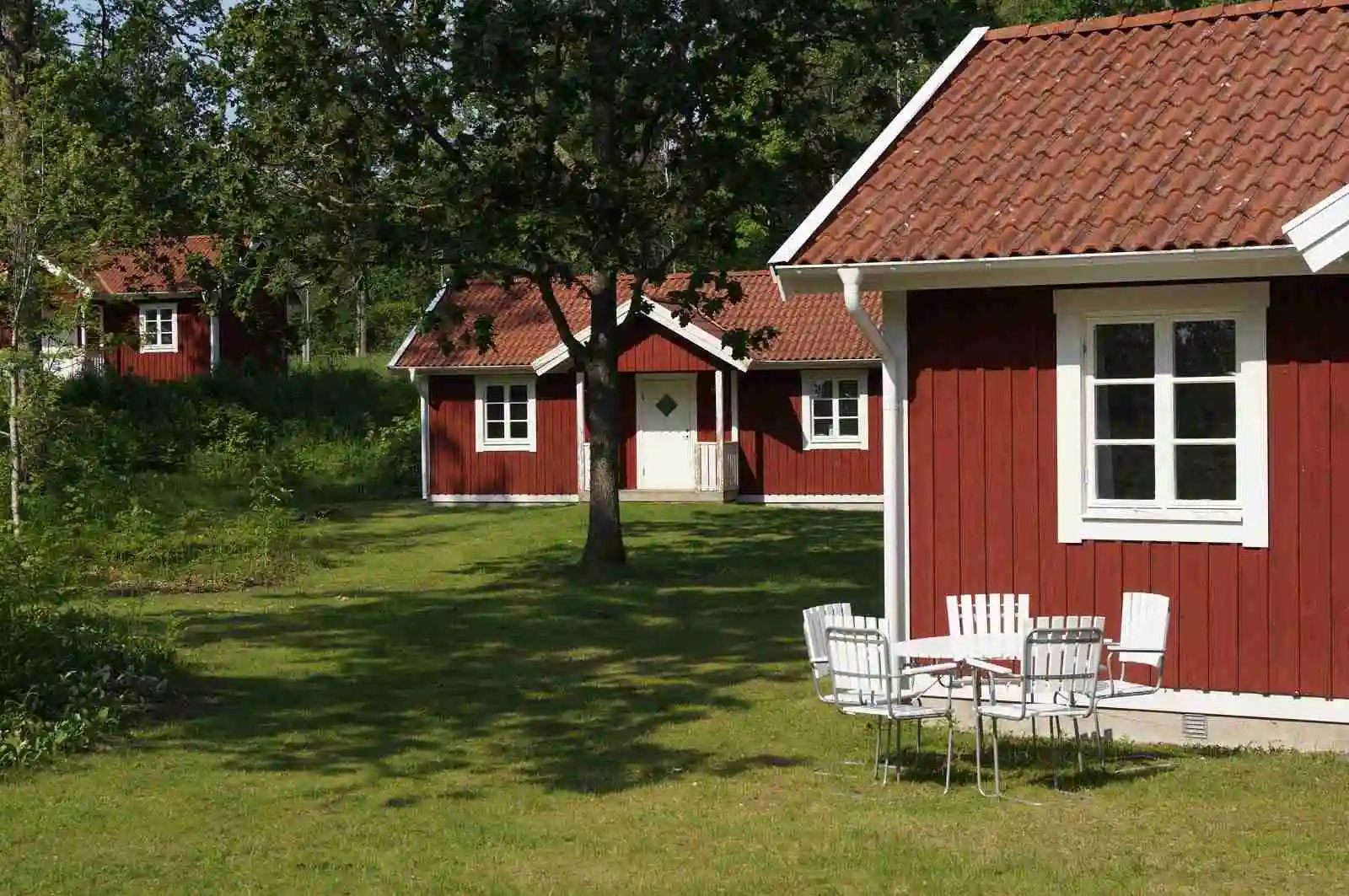 En rofylld bild av Tingsryd Resort visar en lantlig stuga med grästak, omgiven av frodig gräsmatta och buskar.