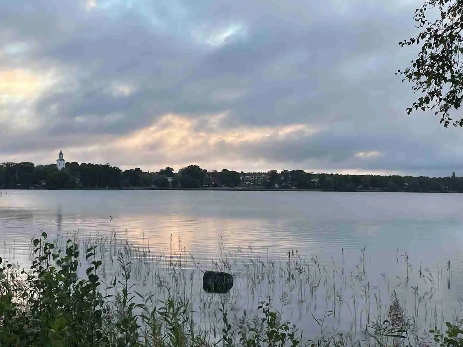 En lugn vattenyta under en blå himmel med moln vid Tingsryd Resort, omgiven av naturskön miljö.