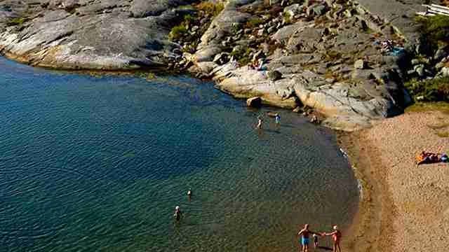En naturskön somrig kustlinje vid Stocken Camping med klippor och en sandstrand som sträcker sig längs vattnet. Perfekt för rekreation och avkoppling vid havet.