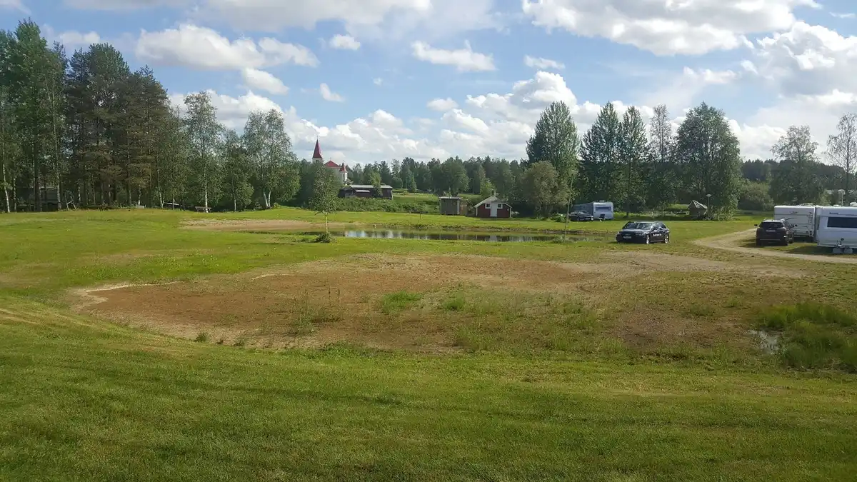 En vidsträckt gräsbevuxen äng vid Fällfors camping, omgiven av moln på en klar himmel, med naturen som sträcker sig över ett landskap av öppna fält och växtlighet.