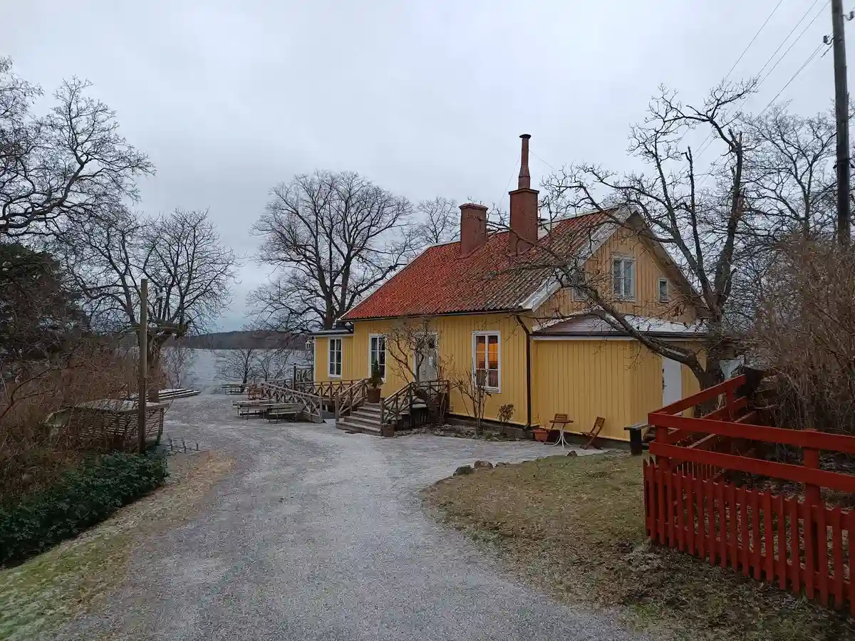 En lantlig stuga vid vatten i ett historiskt område, omgiven av lummig grönska och en stilla sjö.