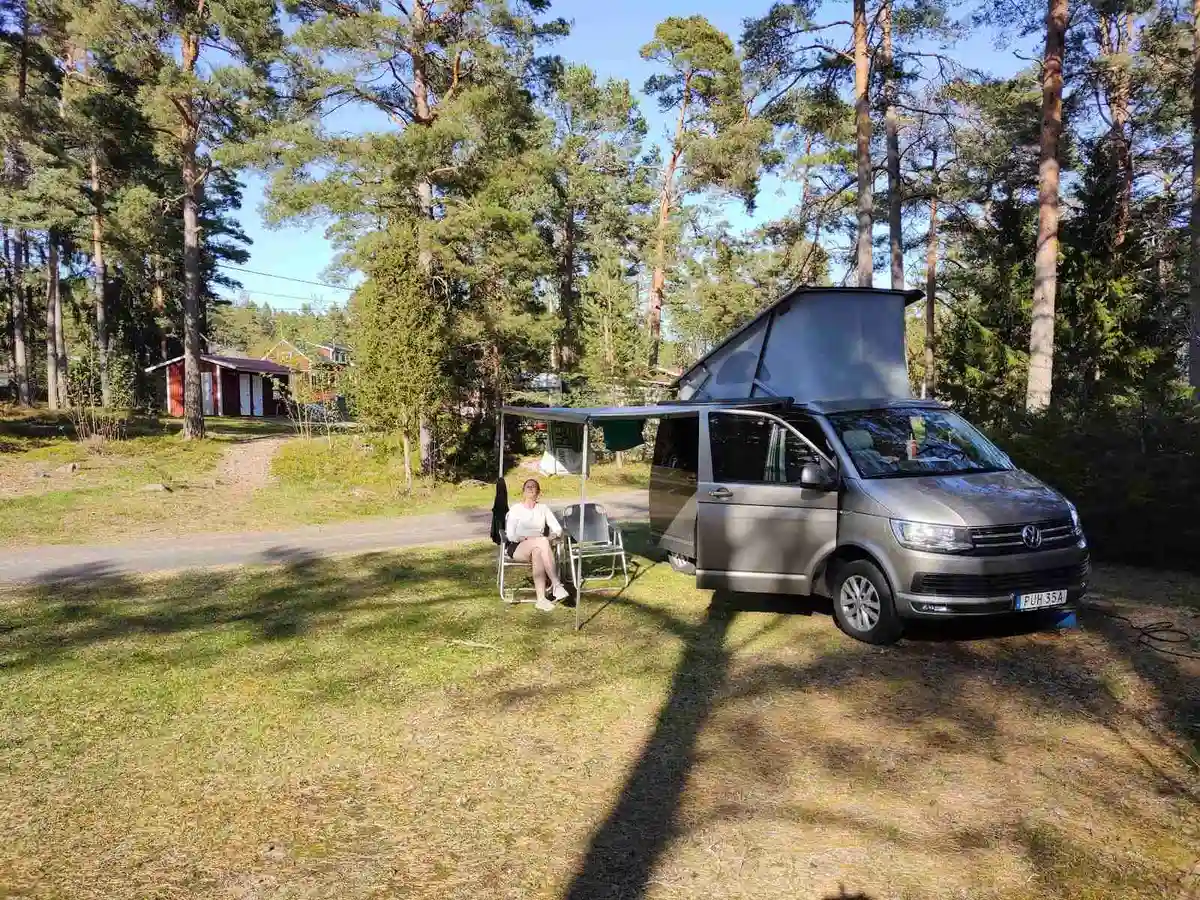 En minivan parkerad vid Norrtälje campingens entré, med tält och bilar i bakgrunden under en klar himmel.