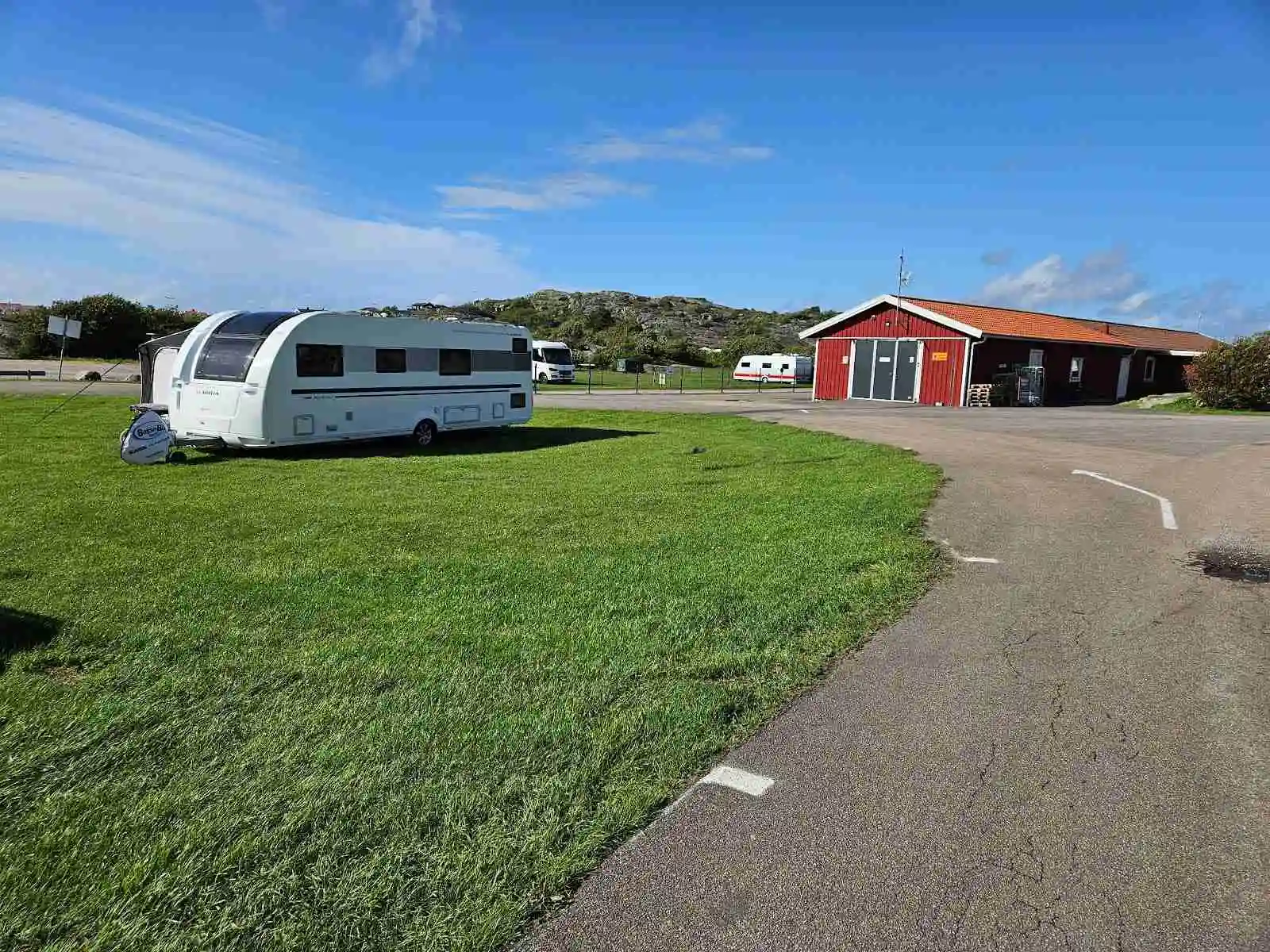 En husbil parkerad på en grön campingplats med en bakgrund av träd och en blå himmel, vilket ger en inbjudande atmosfär för camping och naturupplevelser.