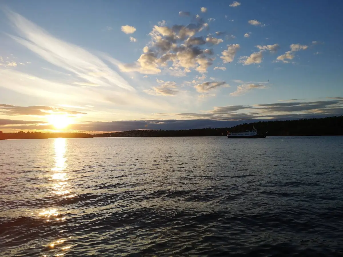 En klarblå himmel med lätta moln hänger över en vidsträckt vattenspegel vid Klubbensborg. I horisonten möts himmel och vatten i en rofylld naturscen.