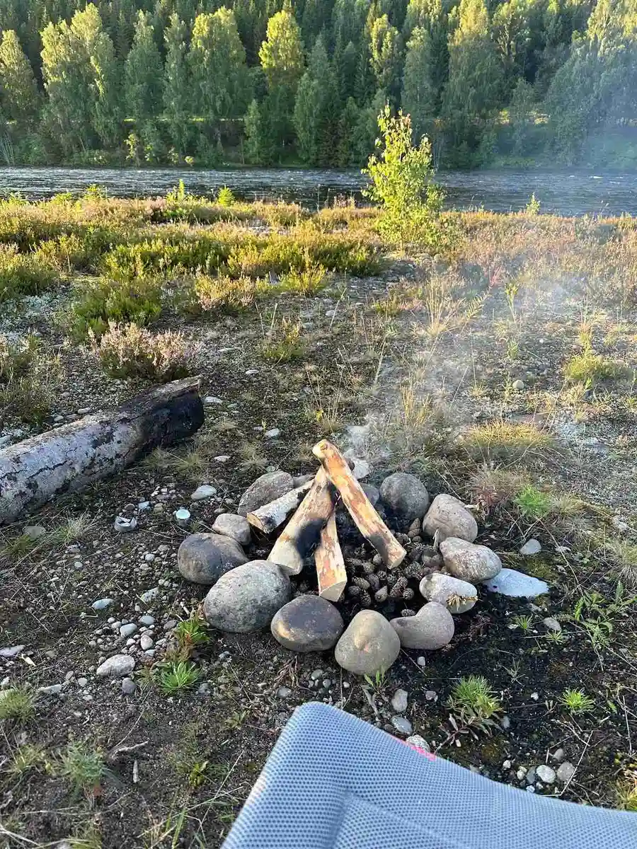 En lägereld omgiven av småsten vid bråtens camping, inbäddad bland barrträd.