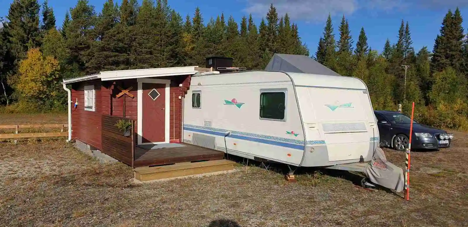 En husbil och en husvagn parkerade vid Storsjö camping och ställplats, omgivna av grönska och träbyggnader.