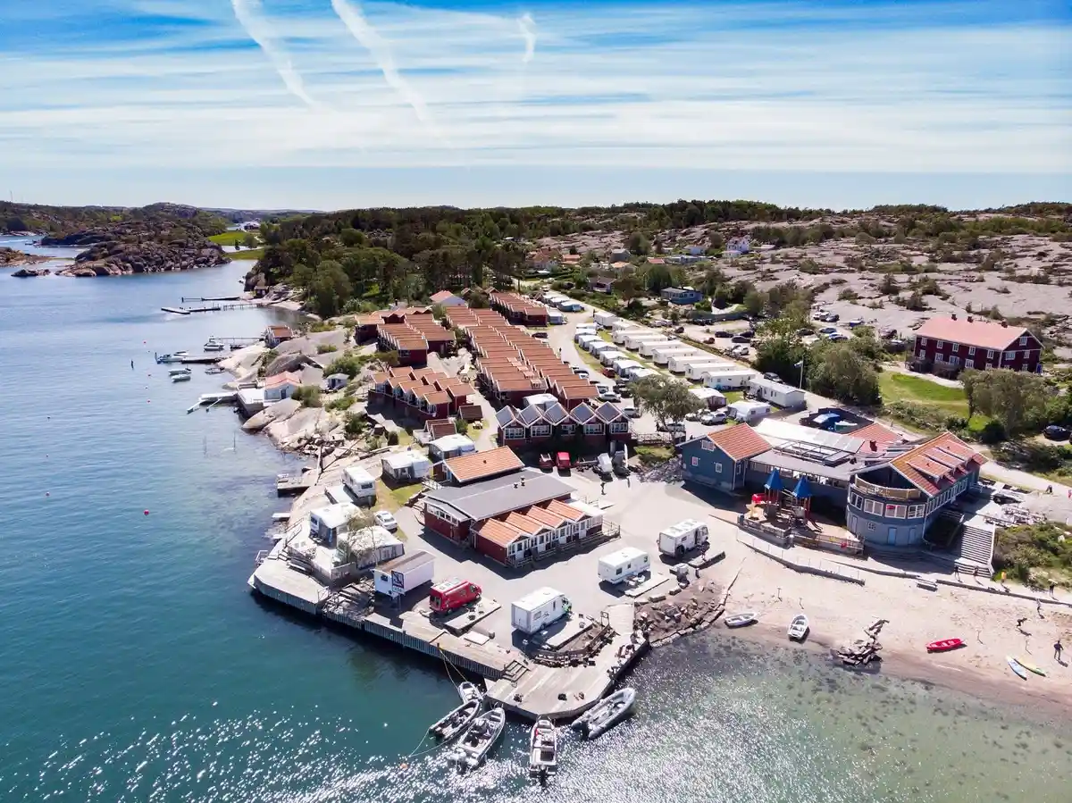 En kustnära stugby och campingplats vid havet, med flera stugor och hus utspridda längs kusten, omgiven av marina och naturliga klimat. Fritidsanläggningen har en brygga och ligger i en naturskön miljö som erbjuder en avkopplande upplevelse, idealisk för en semester i ett kustresortområde.
