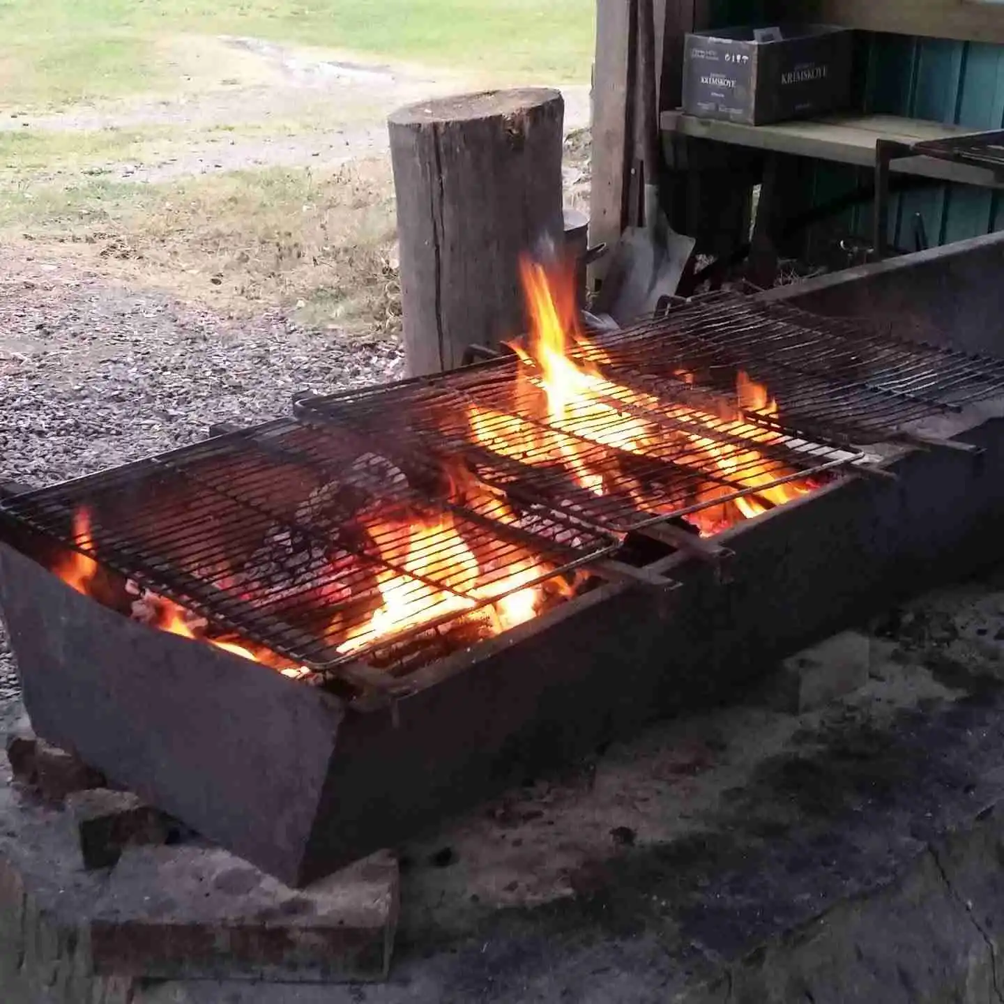 En grill fylld med kött under tillagning på Arkösunds camping, omgiven av flammor och aska.