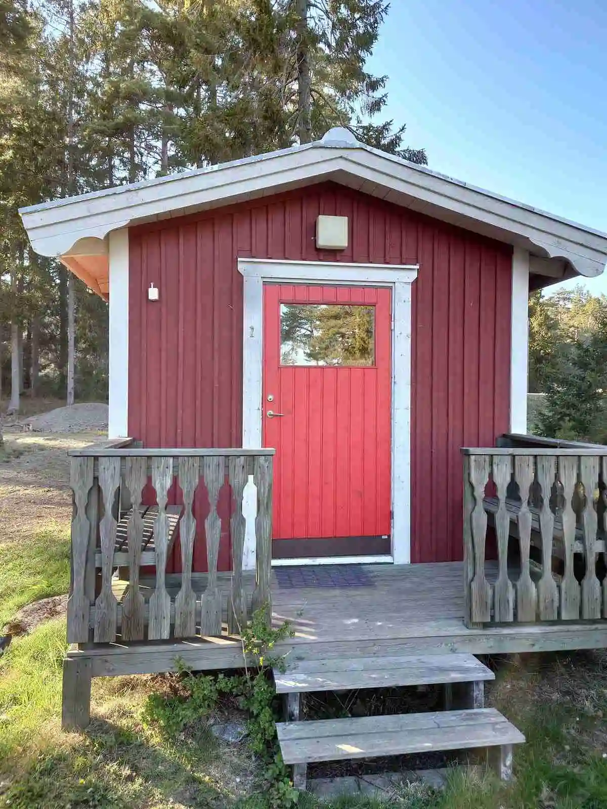 En trästuga med dörr och fönster, omgiven av grönska, belägen vid Norrtälje Camping.