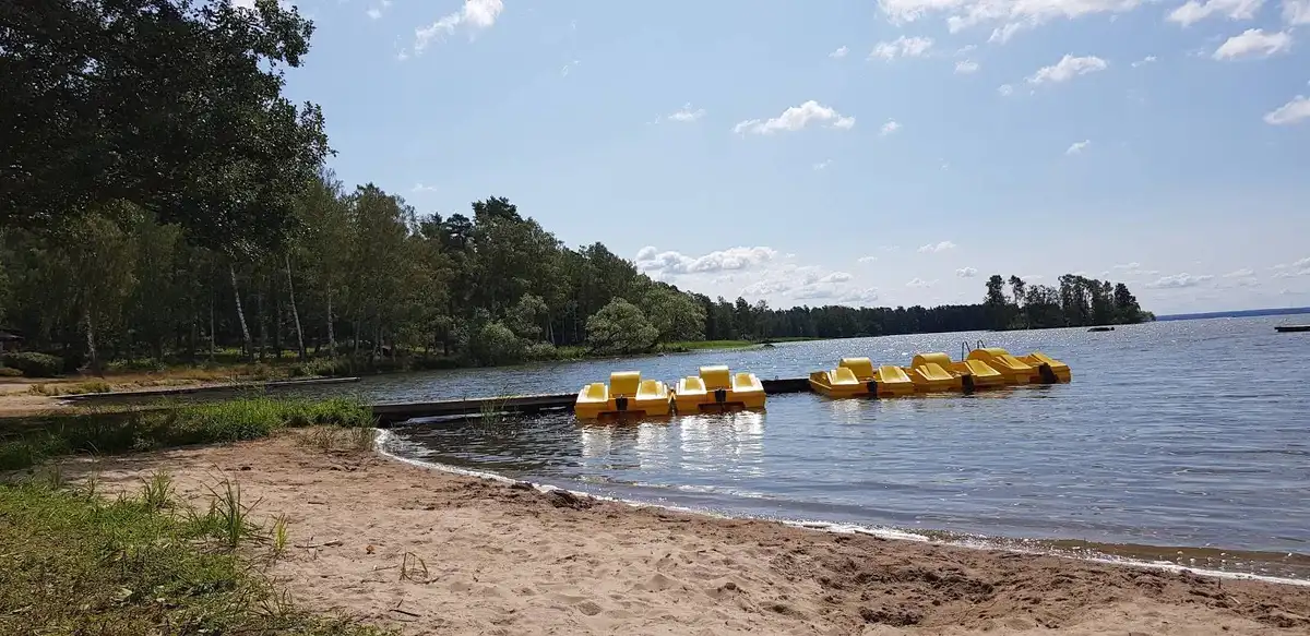 En stilla sjö med en båt som flyter nära strandkanten, omgiven av grönska och träd längs vattendragets bredder.