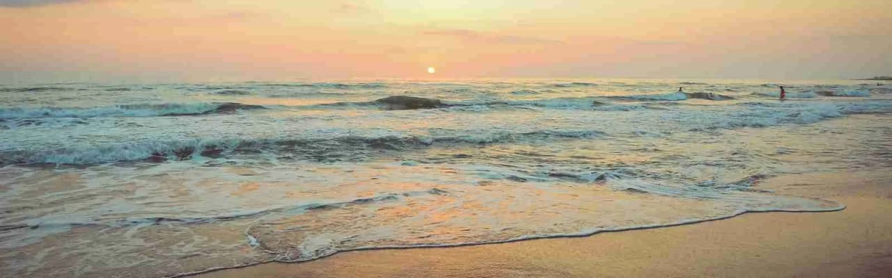 En lugn strand vid Bingsmarkens camping i solnedgången, med havets vågor mot sanden och en färgrik horisont i bakgrunden.