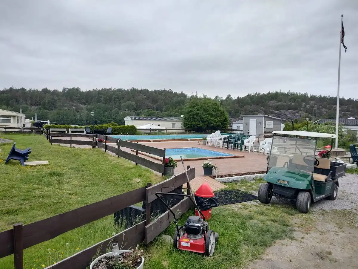 En grönskande campingplats med välskött gräsmatta och landskapsarkitektur. I bakgrunden syns en parkeringsplats med flertalet fordon parkerade.