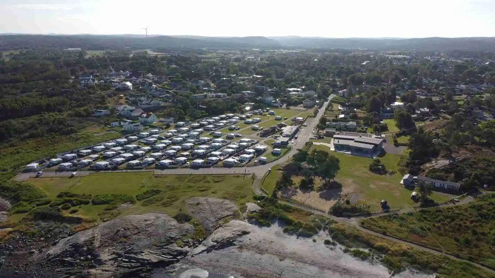 Alt-text: Vy över Vallersvik Camping och Hostel, visar ett pittoreskt landskap med tält uppsatta i närheten av en bostadsby, omgivet av grönskande parkmiljö.