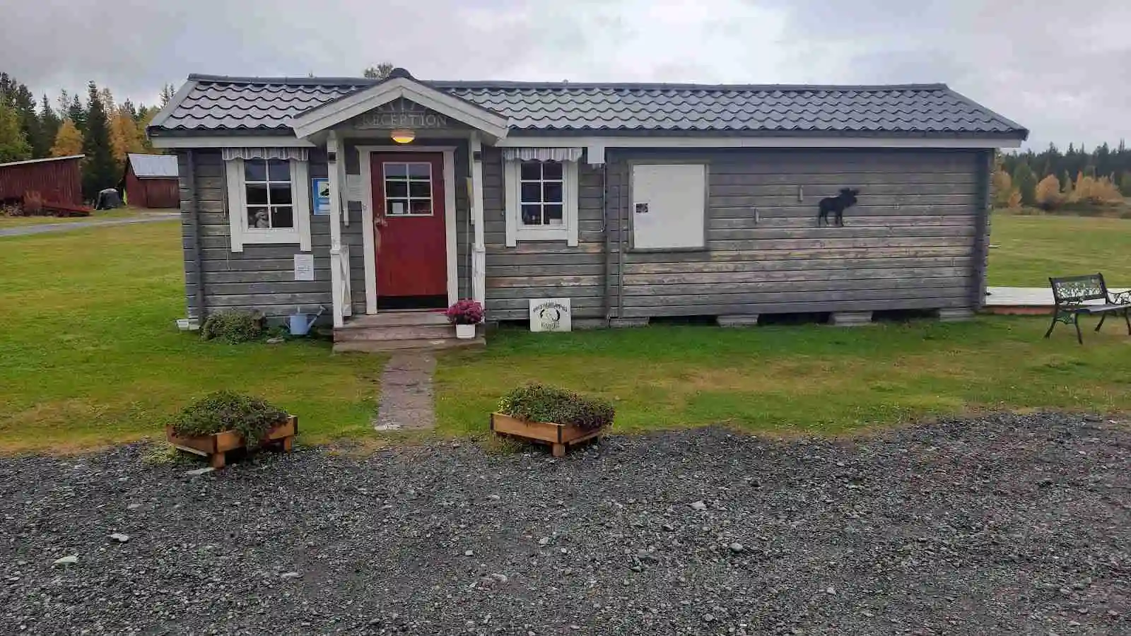 En liten stuga vid Emils fiskecamp omgiven av en välskött trädgård med gröna ytor och en bod i bakgrunden.