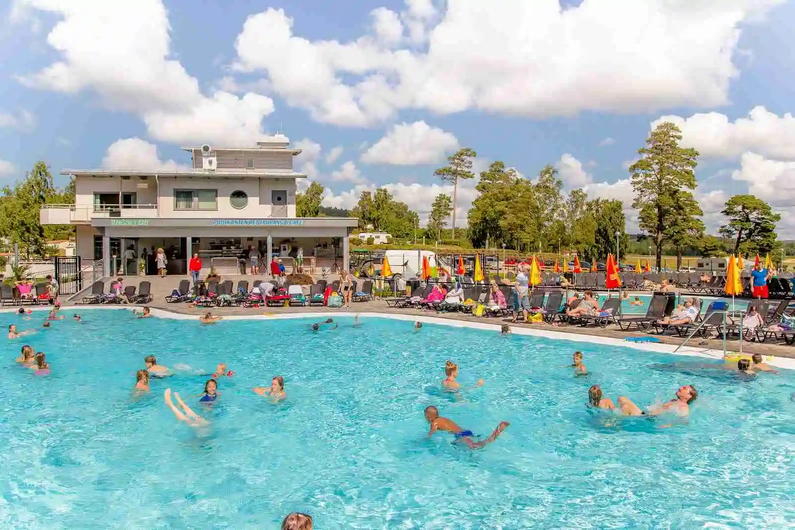 Bild av ett semesterparadis där människor njuter av en simbassäng på Hafsten Resort & Camping. Personen simmar i poolen omgiven av grönskande natur och semesterfaciliteter. Stämningen är avslappnad och inbjudande, perfekt för avkoppling och nöje.