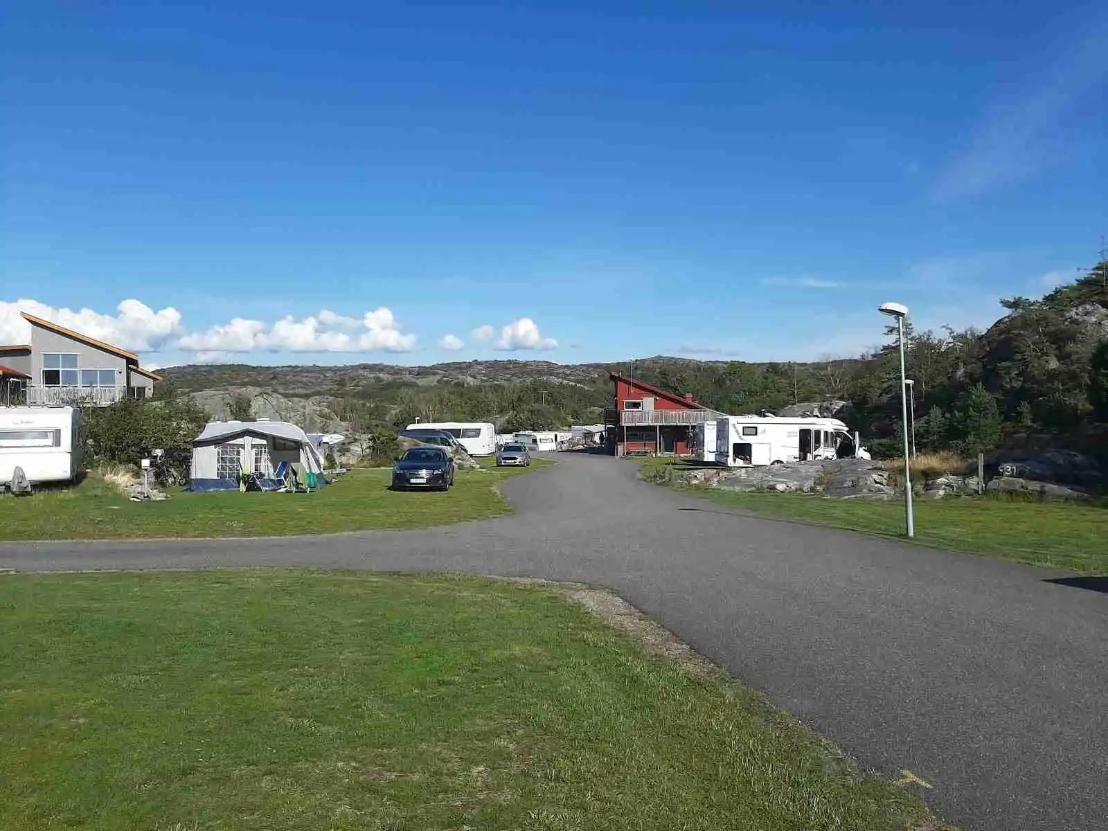 En molnig dag vid Hav & Logi Skärhamn med picnicbord och parkeringsyta. En skåpbil står parkerad bredvid en grusväg och en stolpe, omgivna av en naturskön plats.